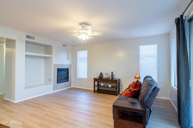 living room featuring ceiling fan, plenty of natural light, light hardwood / wood-style flooring, and a tiled fireplace