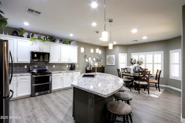 kitchen with pendant lighting, white cabinetry, appliances with stainless steel finishes, and an island with sink