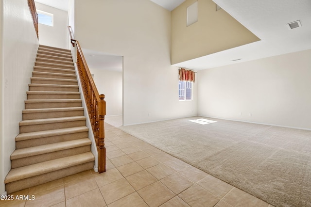 stairs with visible vents, baseboards, carpet, a towering ceiling, and tile patterned floors