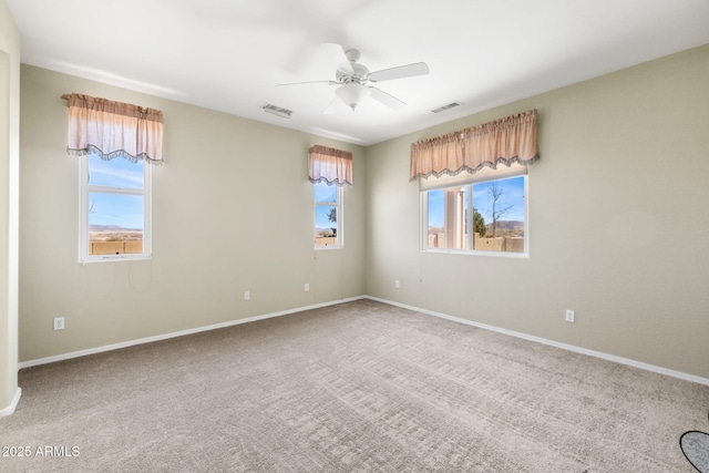 carpeted spare room with visible vents, plenty of natural light, and a ceiling fan