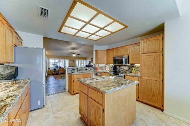 1704 S Barkley Rd, Apache Junction, AZ 85119 - kitchen with appliances with stainless steel finishes, a peninsula, a center island, backsplash, and light stone countertops