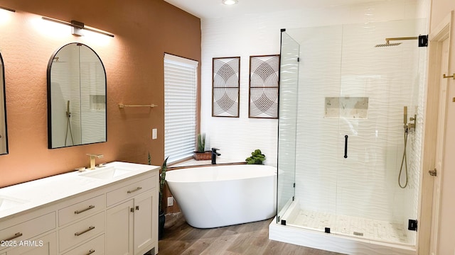 bathroom with double vanity, a soaking tub, wood finished floors, a shower stall, and a sink