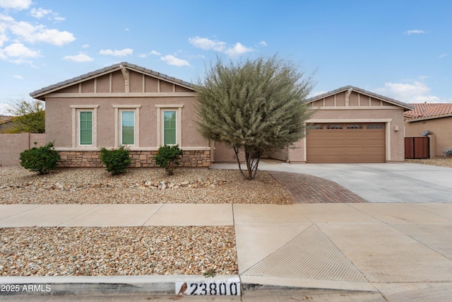 view of front of house with stucco siding, driveway, a tile roof, stone siding, and an attached garage