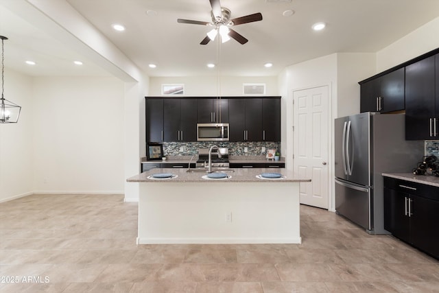 kitchen featuring a sink, appliances with stainless steel finishes, dark cabinets, and a center island with sink