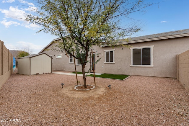 back of house with a fenced backyard, stucco siding, a storage unit, and an outdoor structure