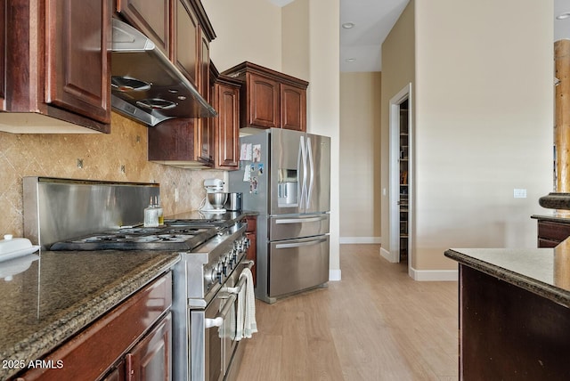 kitchen with backsplash, light hardwood / wood-style flooring, stainless steel appliances, and dark stone counters