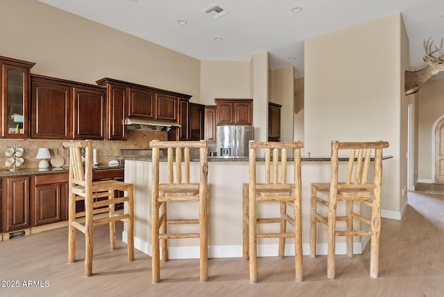 kitchen with backsplash, stainless steel fridge, a breakfast bar area, and stone countertops