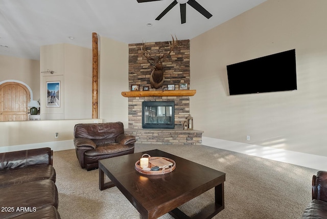 carpeted living room with ceiling fan and a stone fireplace