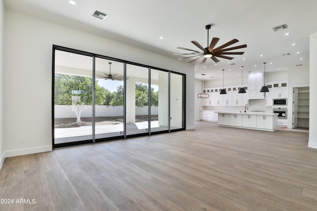 unfurnished living room featuring light hardwood / wood-style floors, sink, and ceiling fan