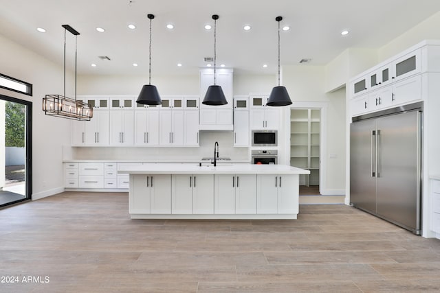 kitchen featuring a large island with sink, built in appliances, pendant lighting, and white cabinetry