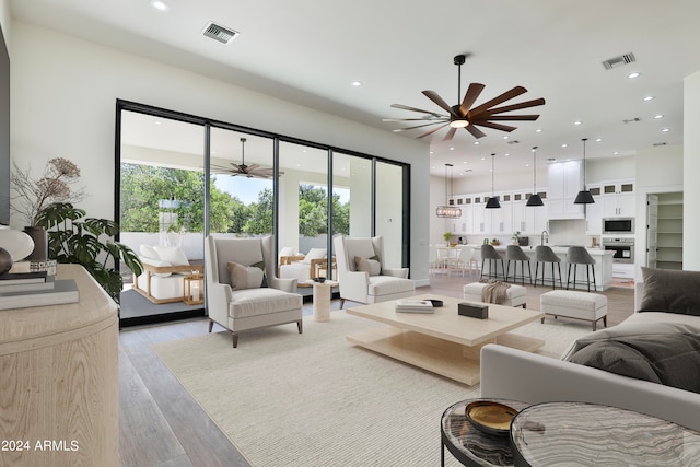 living room featuring ceiling fan, sink, and light wood-type flooring