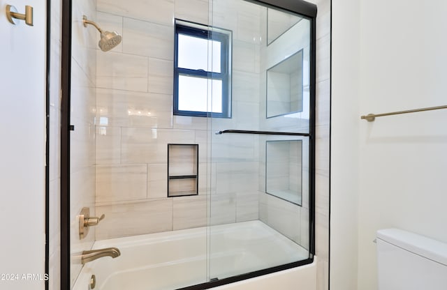 bathroom featuring toilet and bath / shower combo with glass door