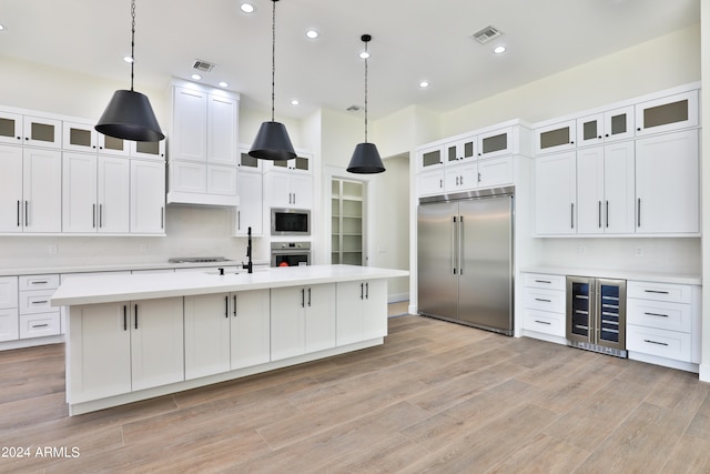 kitchen with built in appliances, light wood-type flooring, an island with sink, and beverage cooler