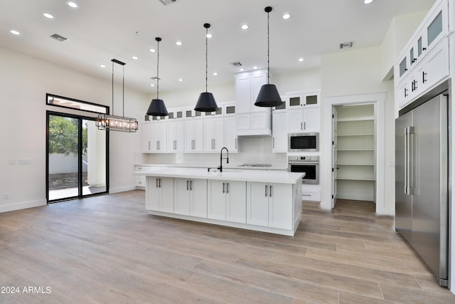 kitchen with an island with sink, decorative light fixtures, stainless steel appliances, and white cabinetry