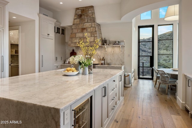 kitchen with wine cooler, tasteful backsplash, light stone countertops, white cabinets, and light wood-type flooring