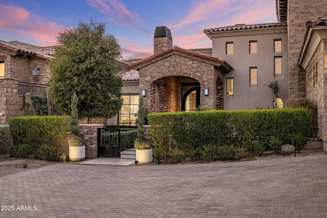 mediterranean / spanish-style home featuring stone siding, a tile roof, fence, and stucco siding