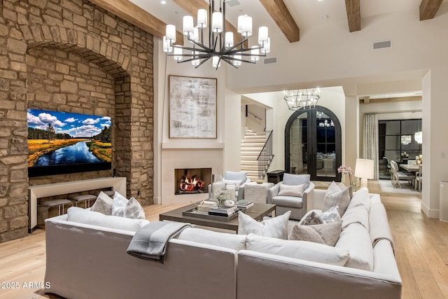 living room with an inviting chandelier, beam ceiling, light hardwood / wood-style flooring, and a high ceiling