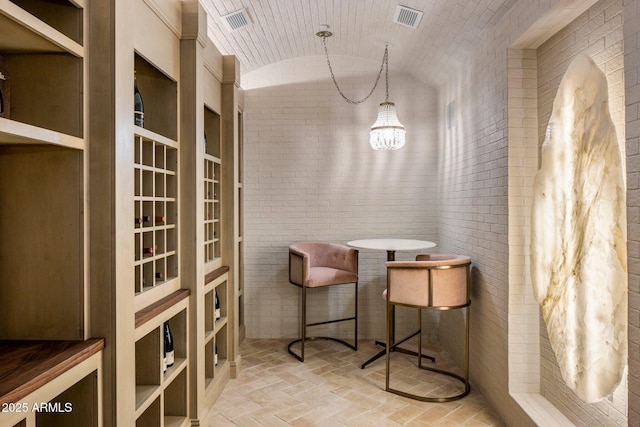 wine area with an inviting chandelier, vaulted ceiling, brick ceiling, and brick wall