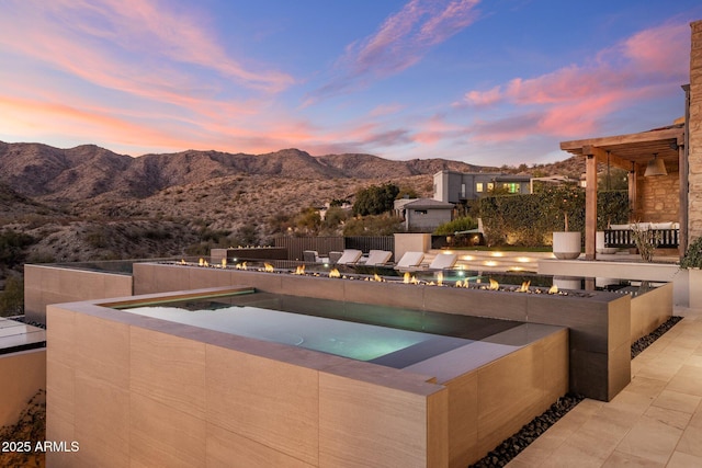 pool at dusk featuring a jacuzzi, a mountain view, and a patio