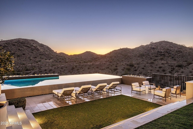 patio terrace at dusk with a mountain view, an outdoor hangout area, a swimming pool, and a lawn