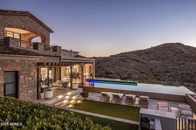 patio terrace at dusk featuring a balcony, a mountain view, and a bar