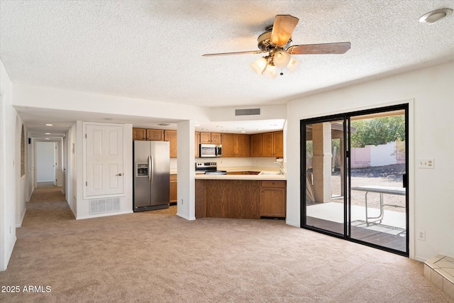 kitchen with brown cabinets, stainless steel appliances, light countertops, visible vents, and light carpet