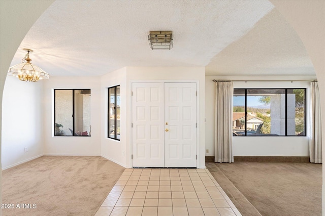 entryway featuring light carpet, light tile patterned floors, arched walkways, an inviting chandelier, and a textured ceiling