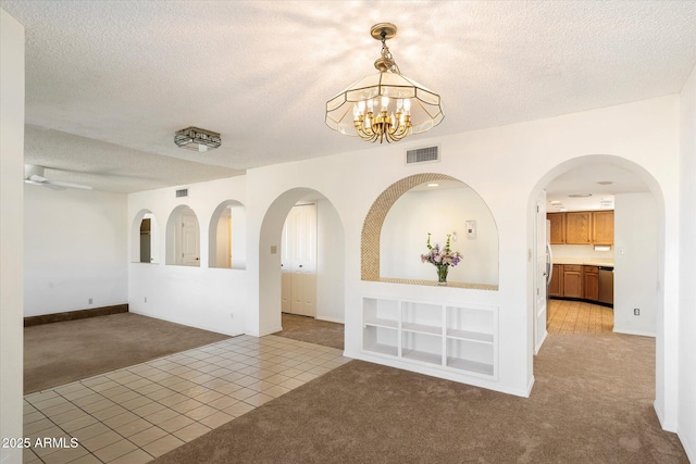 empty room featuring light carpet, an inviting chandelier, visible vents, and a textured ceiling