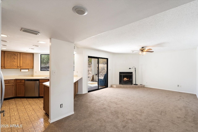 kitchen featuring a lit fireplace, light countertops, a wealth of natural light, brown cabinets, and dishwasher