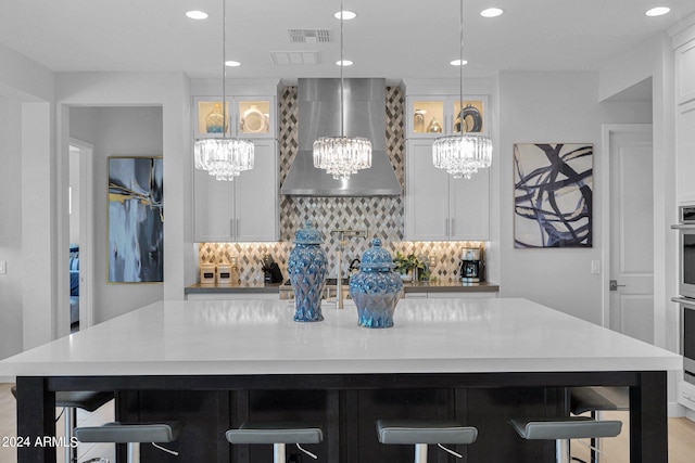 kitchen featuring backsplash, wall chimney range hood, a breakfast bar, hanging light fixtures, and a large island