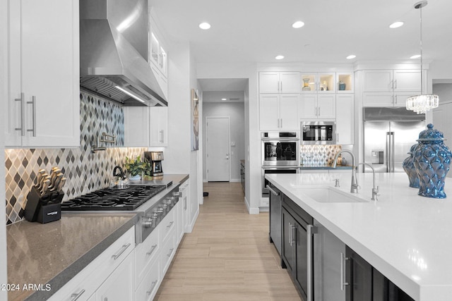 kitchen with decorative light fixtures, sink, island exhaust hood, built in appliances, and white cabinets