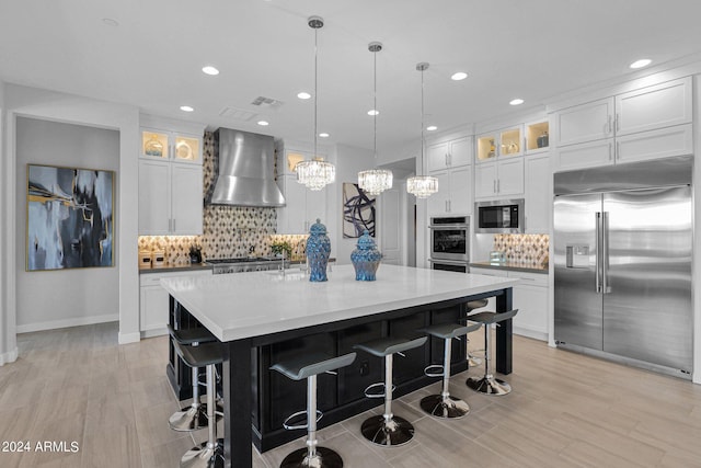 kitchen featuring white cabinetry, wall chimney exhaust hood, a large island, and built in appliances