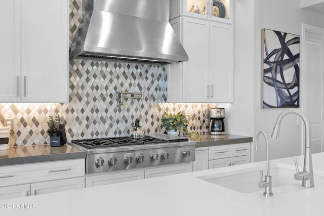 kitchen with stainless steel gas stovetop, wall chimney range hood, decorative backsplash, sink, and white cabinets