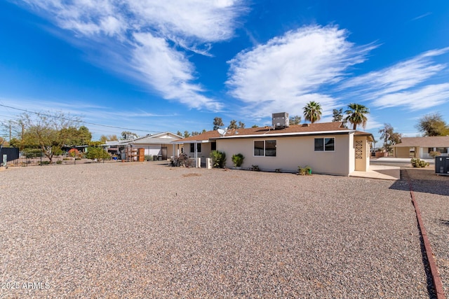 rear view of property with central air condition unit, fence, and stucco siding