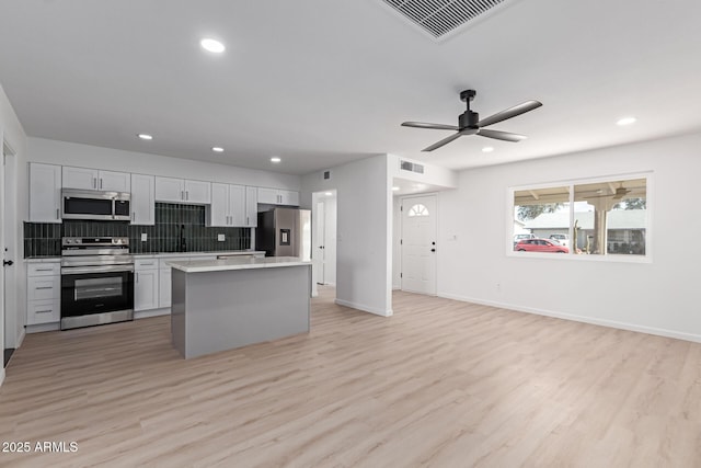 kitchen featuring visible vents, open floor plan, a center island, stainless steel appliances, and light countertops