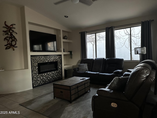 living room featuring a tiled fireplace, lofted ceiling, tile patterned flooring, and ceiling fan