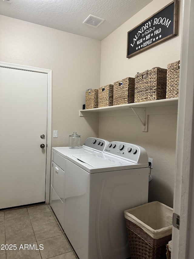 laundry area featuring washing machine and dryer, light tile patterned flooring, and a textured ceiling