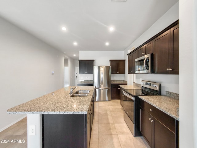 kitchen with light stone countertops, a center island with sink, stainless steel appliances, sink, and dark brown cabinetry