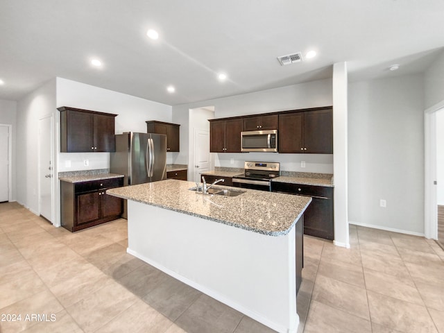 kitchen with an island with sink, light stone counters, sink, and appliances with stainless steel finishes