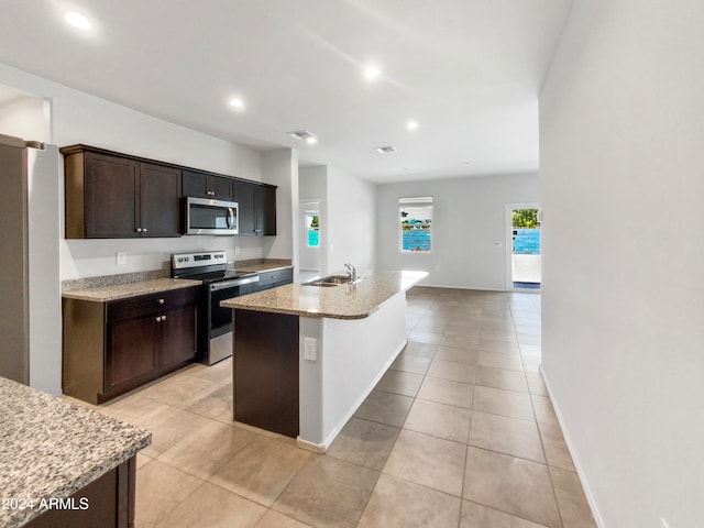 kitchen featuring light stone countertops, stainless steel appliances, sink, dark brown cabinets, and a kitchen island with sink