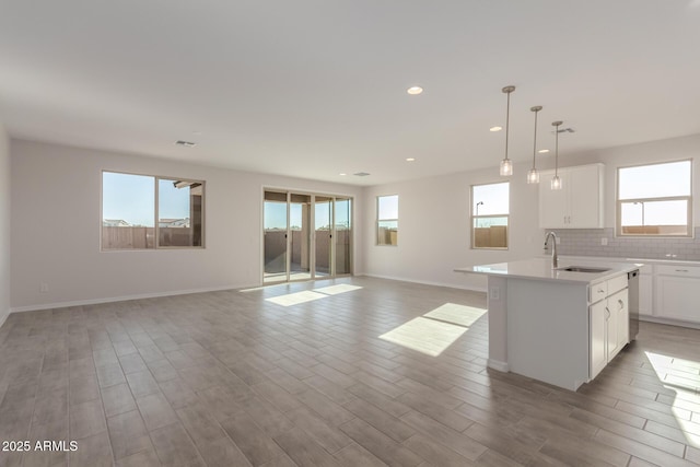 kitchen featuring decorative light fixtures, white cabinetry, sink, backsplash, and a kitchen island with sink