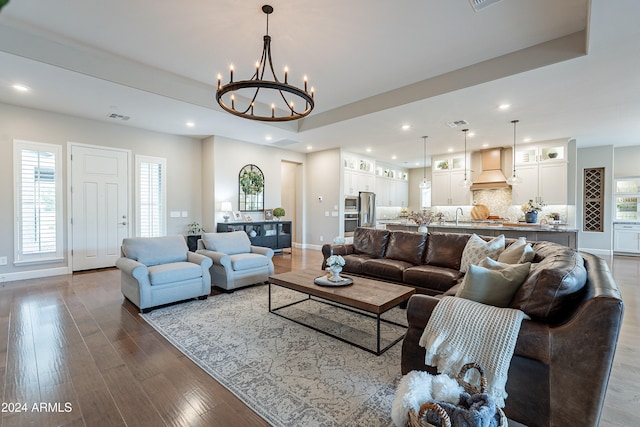 living room with sink, an inviting chandelier, a tray ceiling, and wood-type flooring