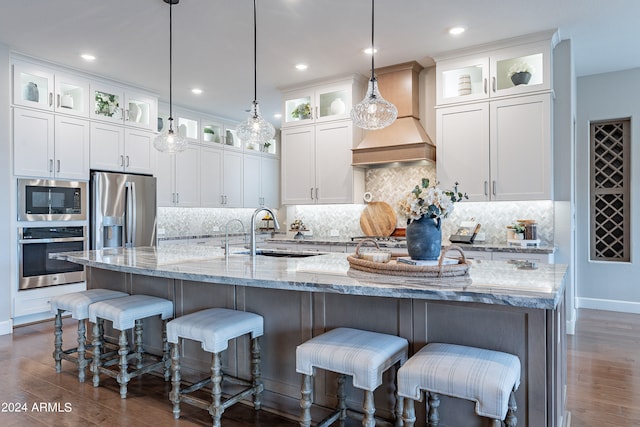 kitchen with appliances with stainless steel finishes, custom range hood, a large island with sink, white cabinets, and dark wood-type flooring