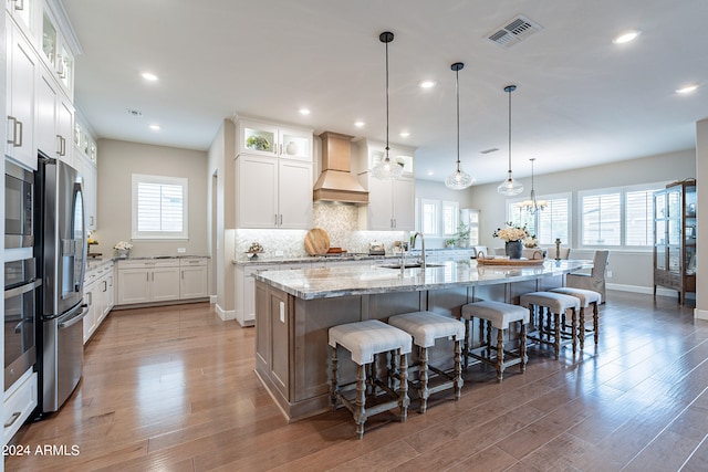 kitchen with a large island with sink, wood-type flooring, plenty of natural light, and premium range hood