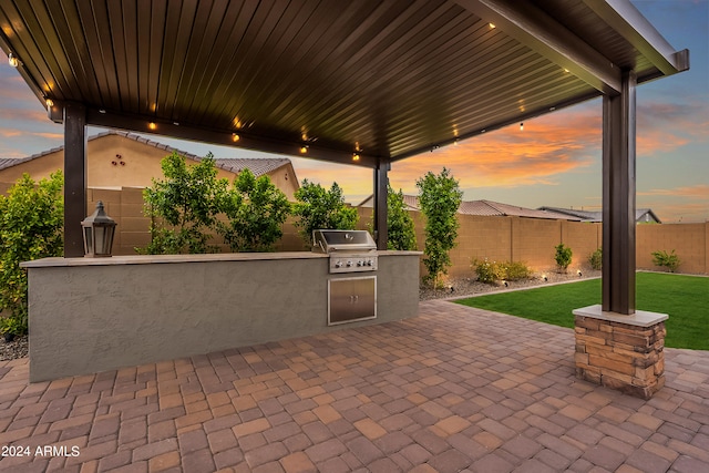 patio terrace at dusk featuring grilling area, exterior kitchen, and a lawn