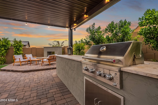 patio terrace at dusk with outdoor lounge area, a grill, and an outdoor kitchen