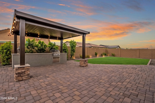 patio terrace at dusk with exterior kitchen, a yard, and grilling area