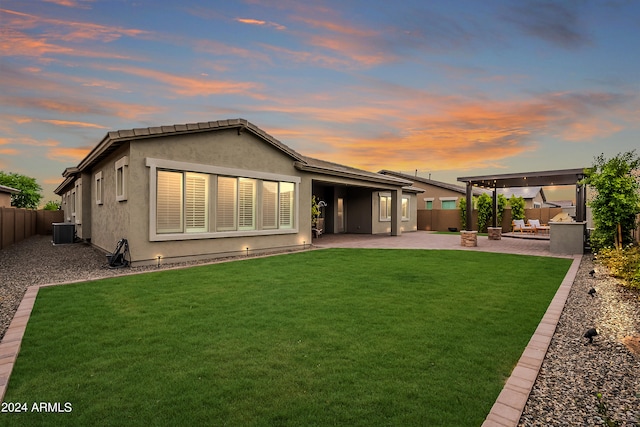 back house at dusk with a lawn and a patio area