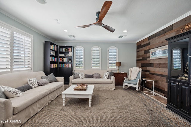 living room with wooden walls, plenty of natural light, ornamental molding, and ceiling fan