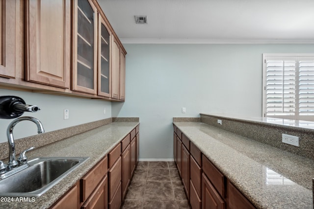 kitchen featuring crown molding, visible vents, glass insert cabinets, baseboards, and a sink